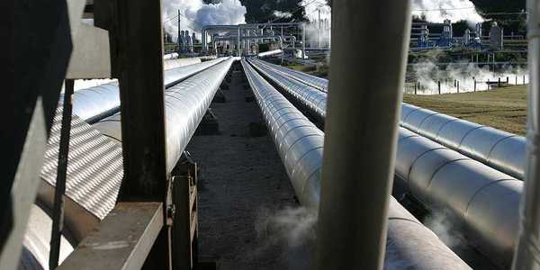 Pipelines extending toward a geothermal energy plant with steam rising from it