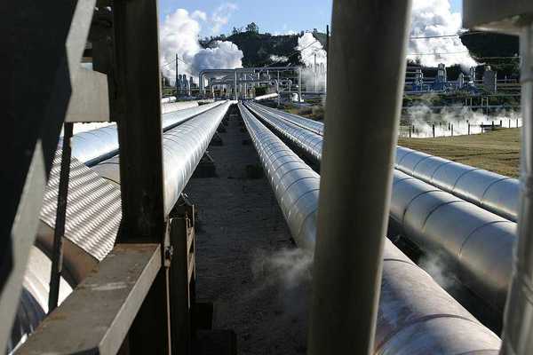 Pipelines extending toward a geothermal energy plant with steam rising from it