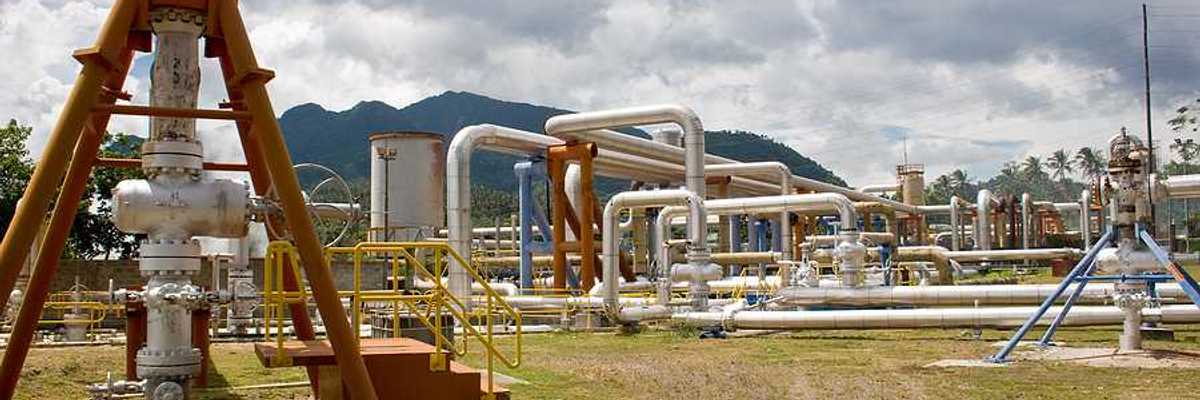 Pipes rising out of the ground at a geothermal well with mountains in the background
