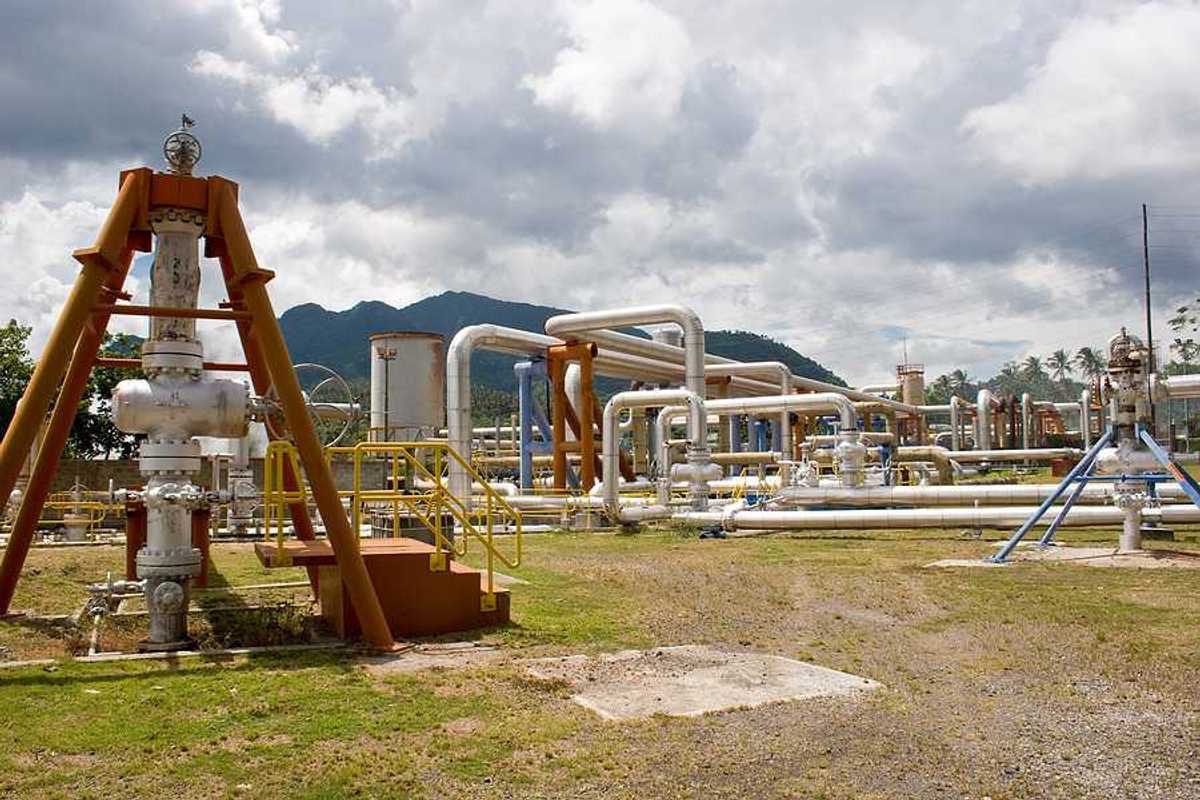 Pipes rising out of the ground at a geothermal well with mountains in the background