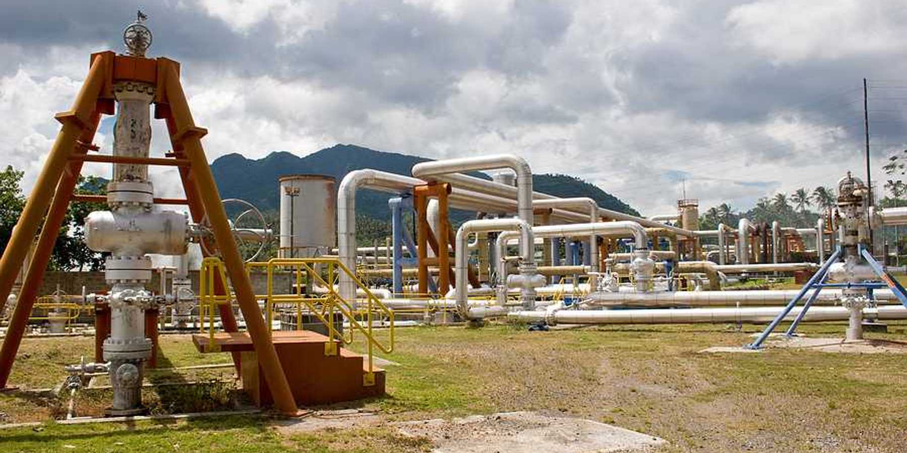 Pipes rising out of the ground at a geothermal well with mountains in the background