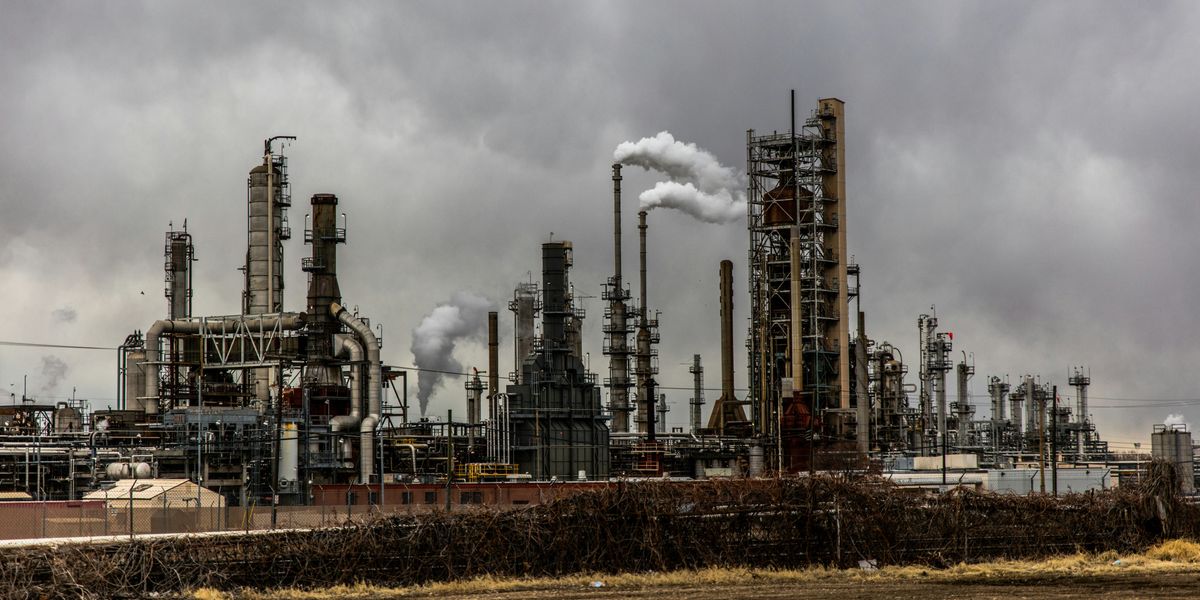Polluting oil refinery emits smoke under cloudy sky.