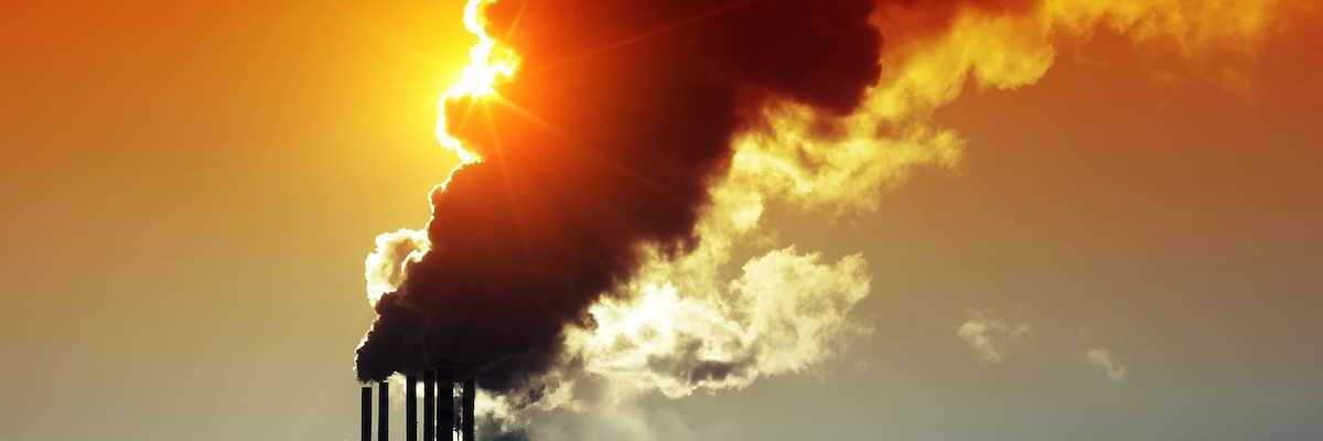 Power plant discharging smoke and dirty orange air obscuring the sun