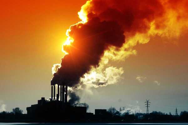Power plant discharging smoke and dirty orange air obscuring the sun