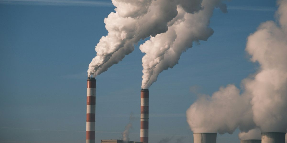 Power plant smokestacks spew white pollution into the sky on a sunny day.