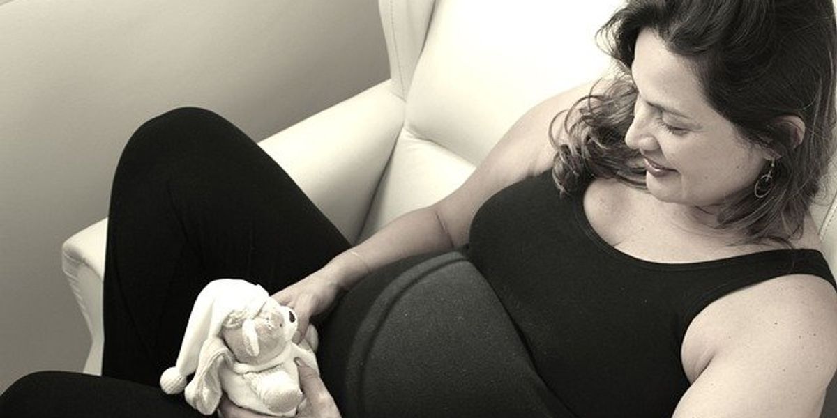 Pregnant woman on sofa holding stuffed toy.