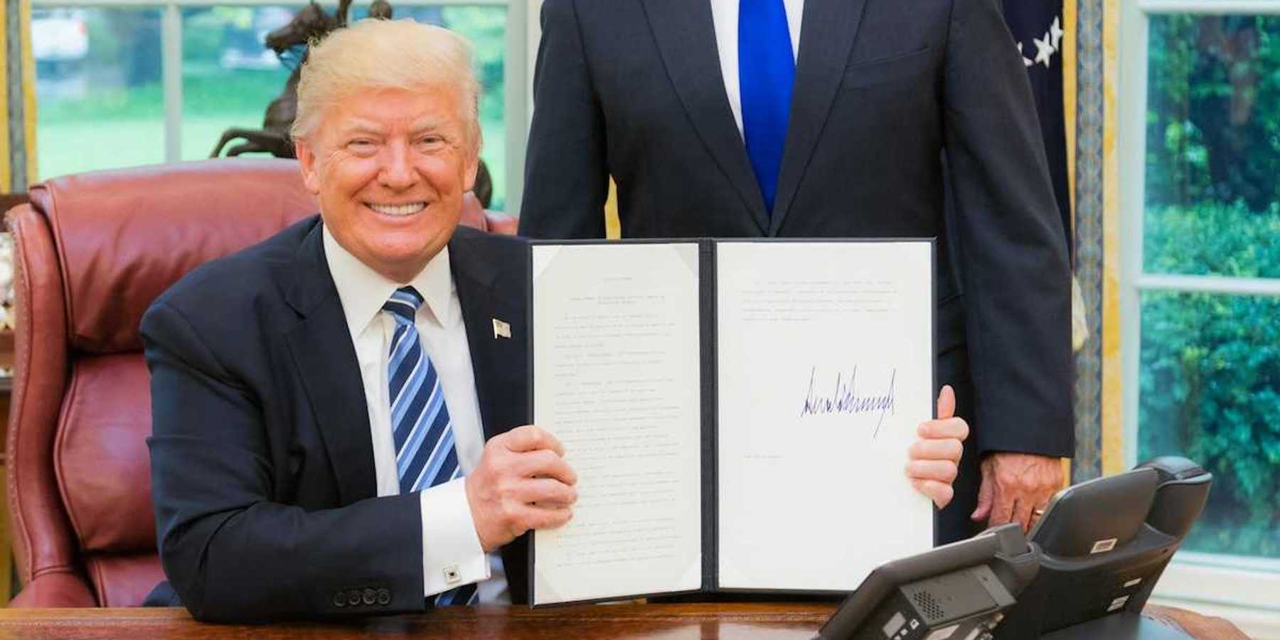 President Trump smiling while displaying a recently signed executive order