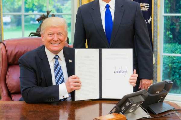 President Trump smiling while displaying a recently signed executive order