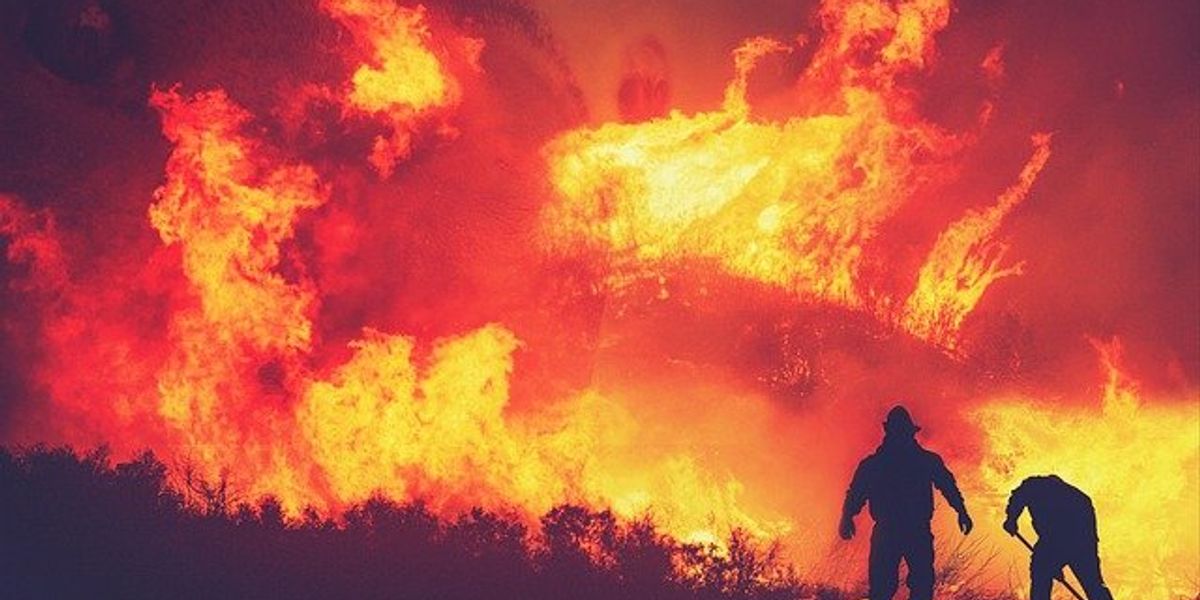 Raging wildfire with silhouette of two firefighters in the foreground.