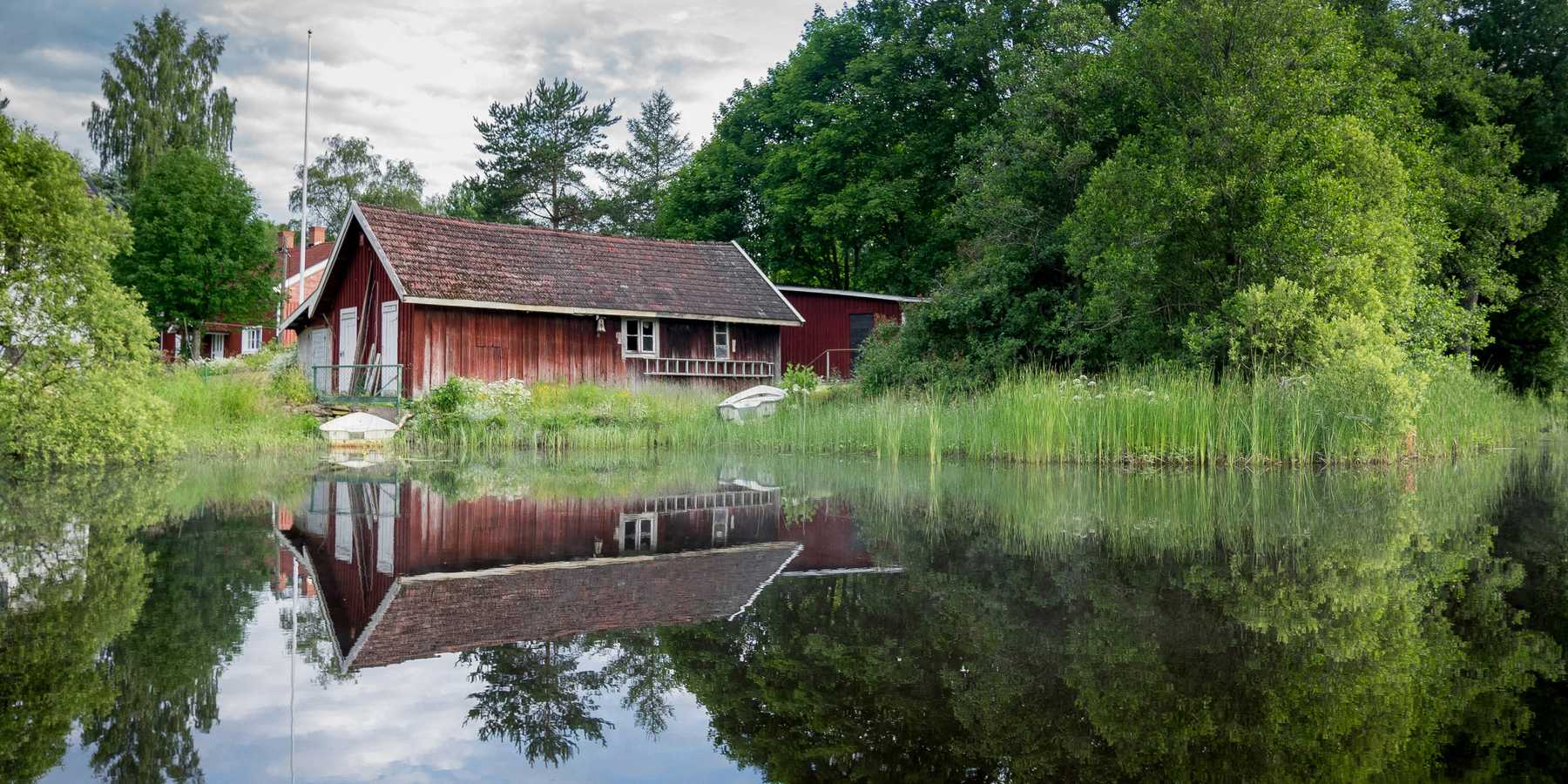 Red barn reflected in a calm pond with a green forest in the background.