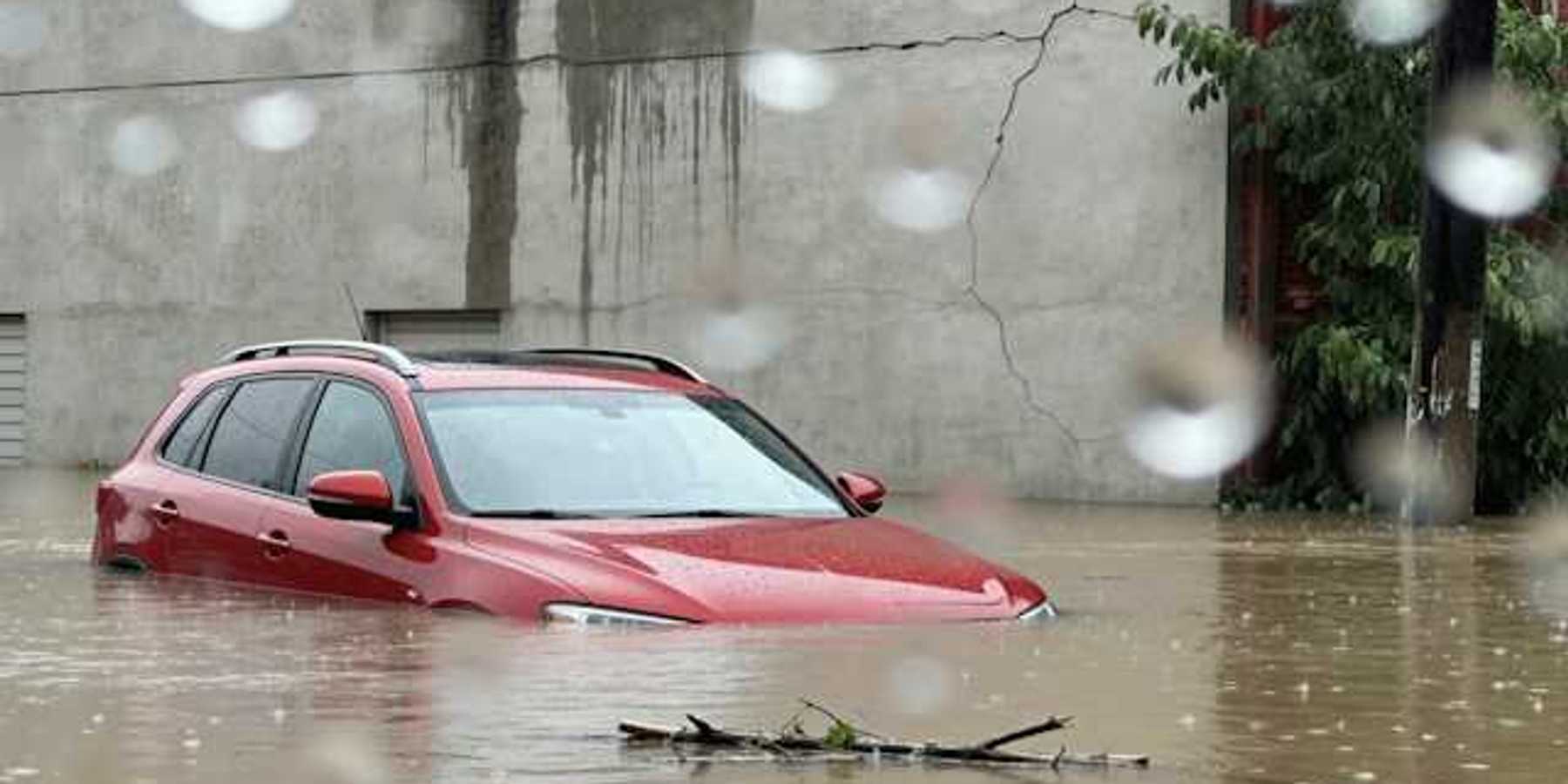 Red car submerged under flood waters with a concrete building behind it