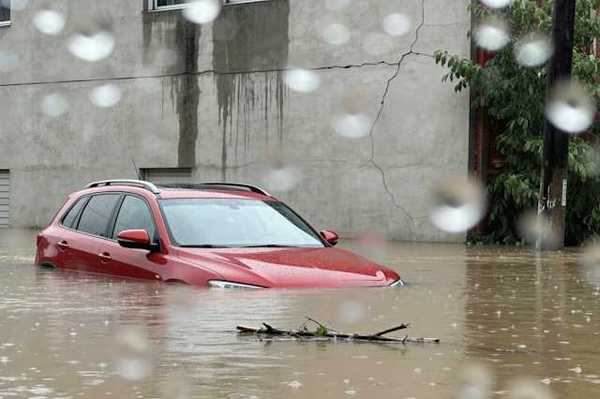 Red car submerged under flood waters with a concrete building behind it