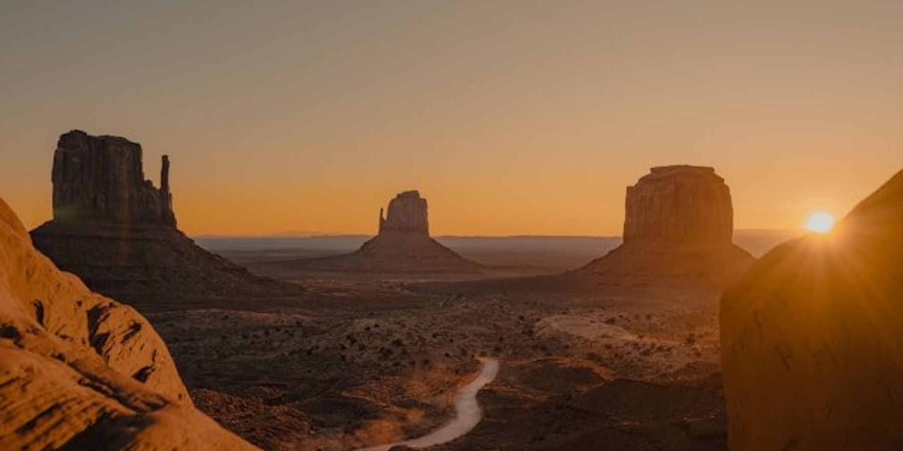 Red rock formations in Monument Valley, Utah under a setting sun.