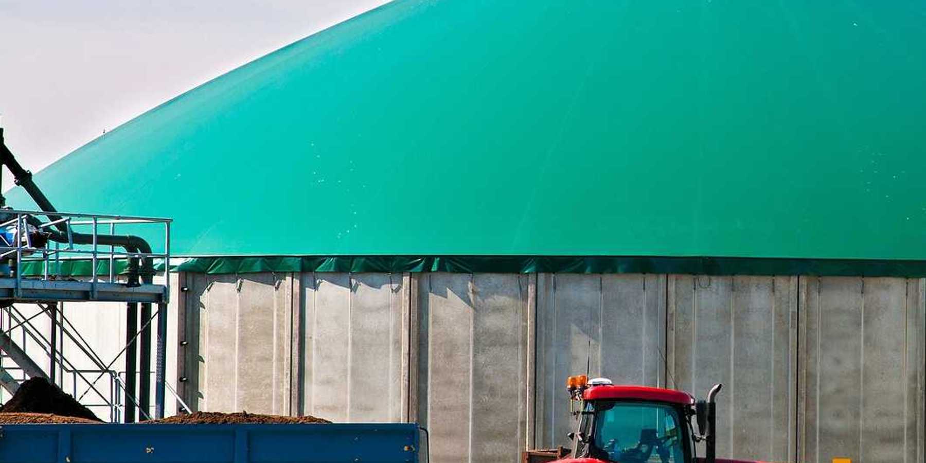 Red tractor hitched to a wagon of manure parked in front of a biogas facility.