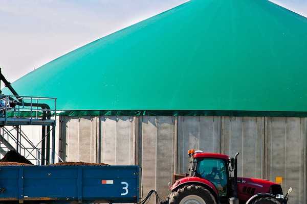 Red tractor hitched to a wagon of manure parked in front of a biogas facility.