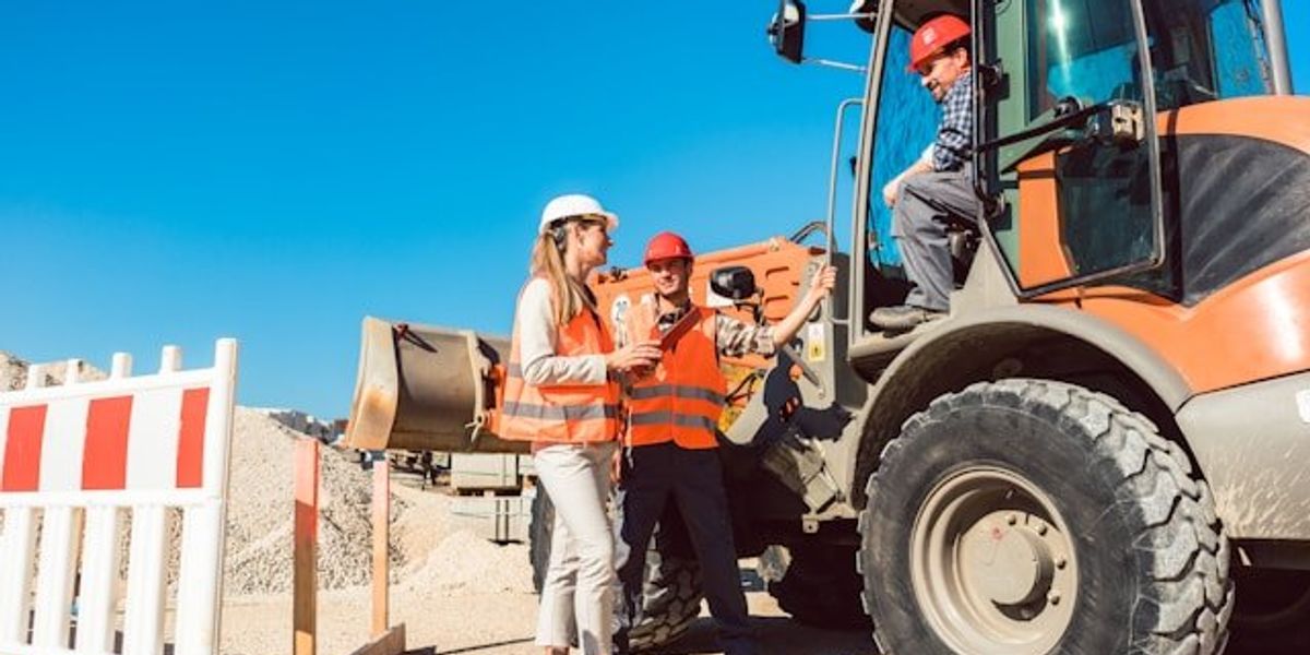 Road workers in red safety vests standing in front of road equipment