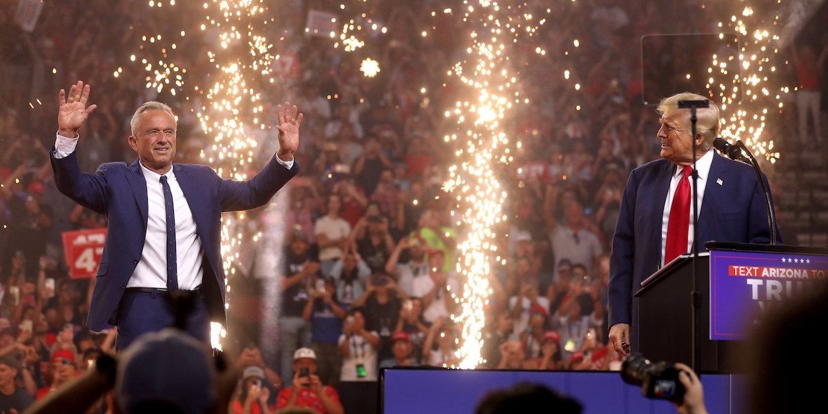 Robert F. Kennedy, Jr. and Donald Trump appear on a stage with fireworks and a crowd in the background.