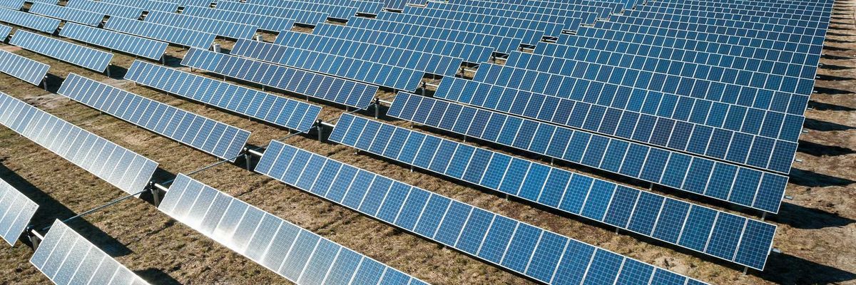 Rows of solar panel boards on brown ground.