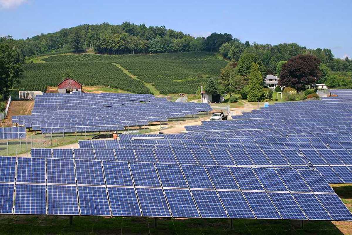 Rows of solar panels stretching up a hill toward a farm field