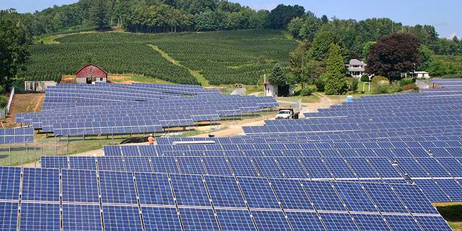 Rows of solar panels stretching up a hill toward a farm field