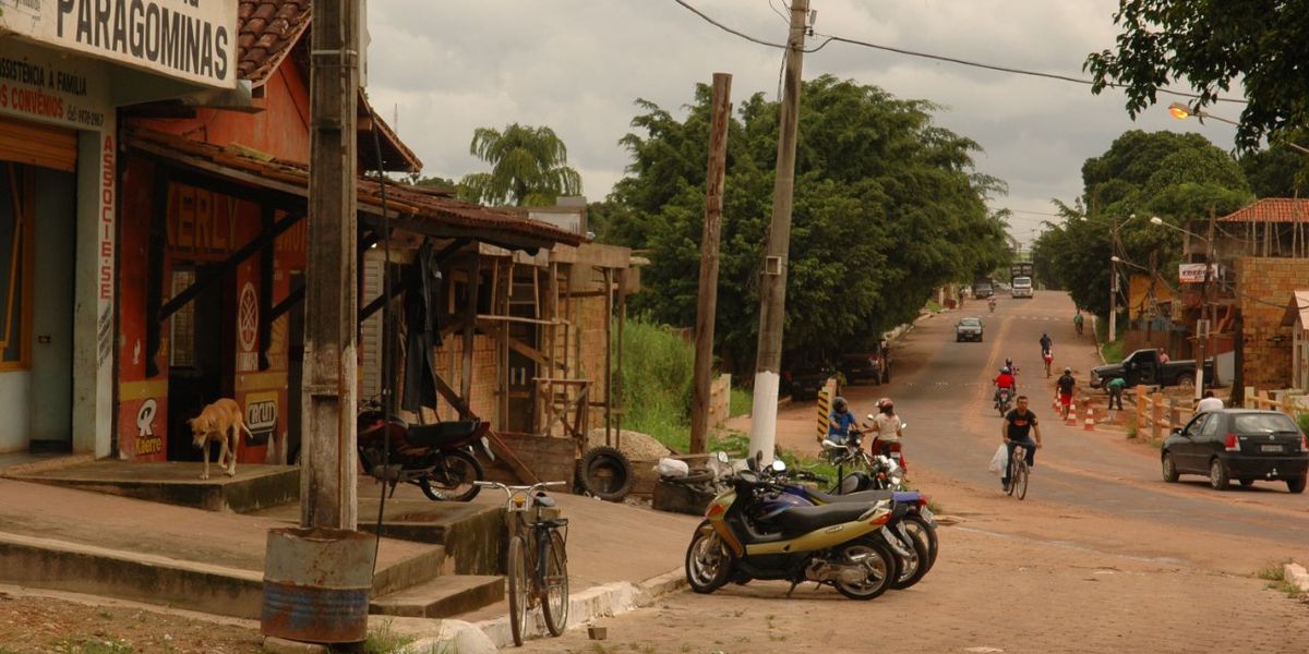 Rural village in the Amazon shows store fronts, motorcycles and people riding bicycles with trees in background.
