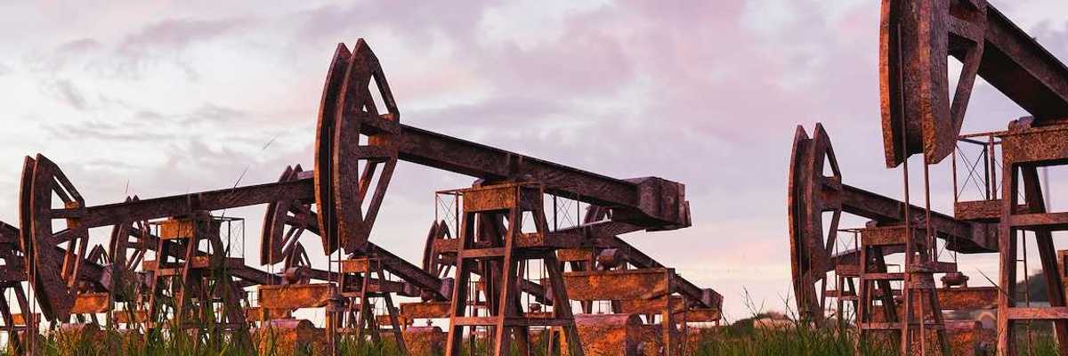 Rusted and abandoned oil pumps with grass growing around it against sunset.