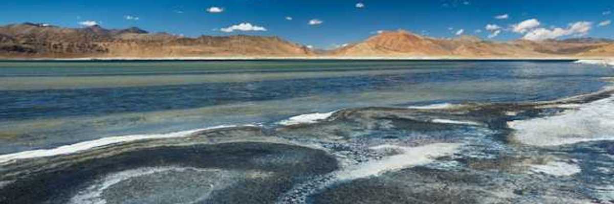 Salt flats in front of a lake with mountains in the distance