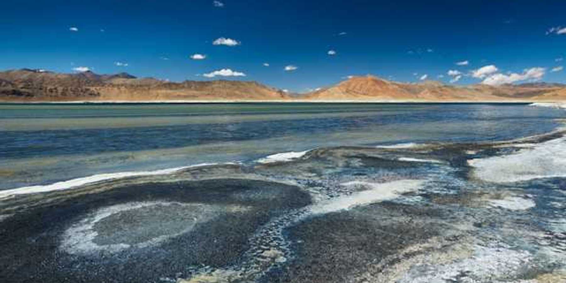 Salt flats in front of a lake with mountains in the distance