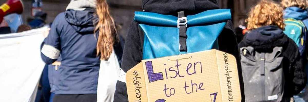 School children march for science with sign on backpack reading "Listen to the Science!"