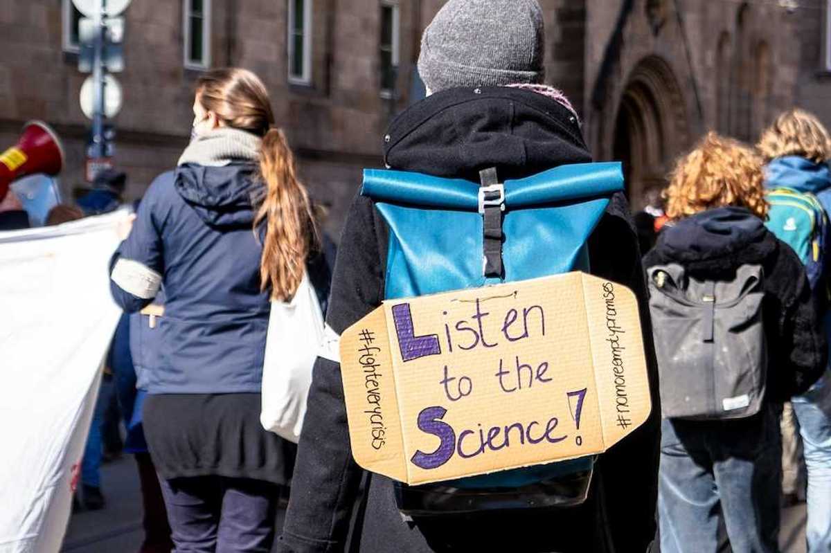 School children march for science with sign on backpack reading "Listen to the Science!"