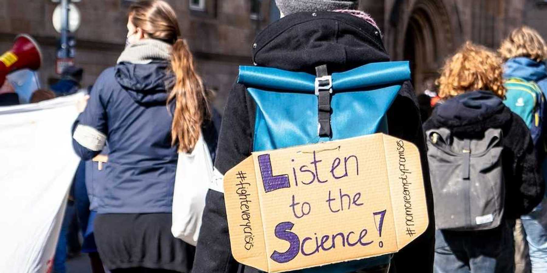 School children march for science with sign on backpack reading "Listen to the Science!"