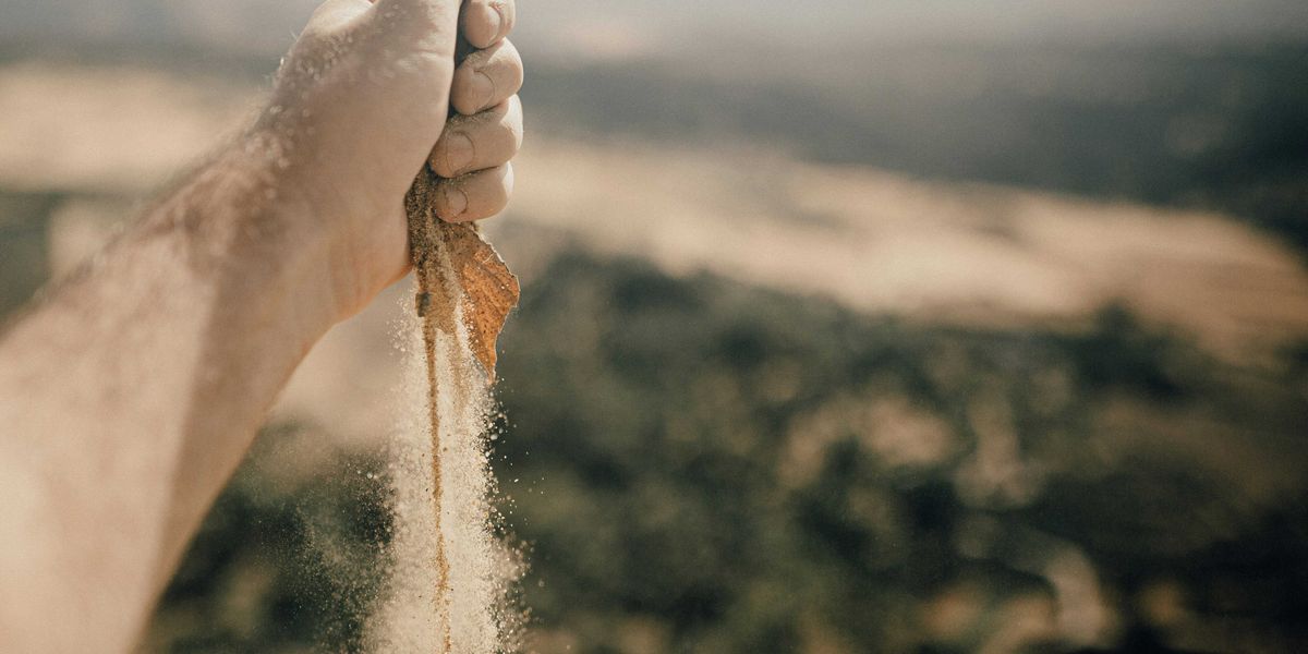 selective focus photography of person with dirt streaming from their hand