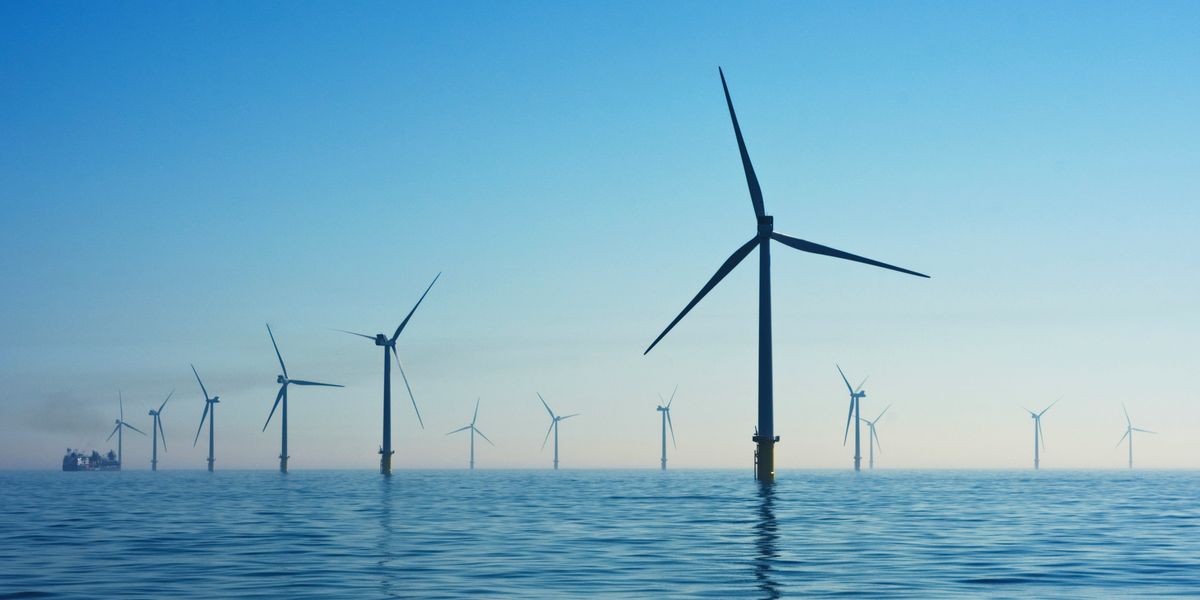Series of wind turbines installed in the ocean with a ship in the background.