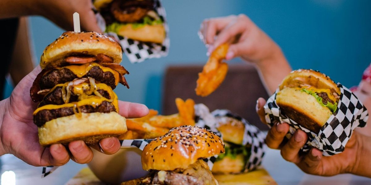 Several hands holding beef cheeseburgers above a tray