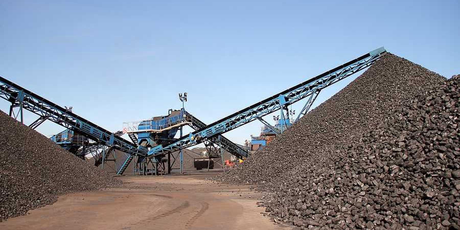Several piles of coal with equipment in the background