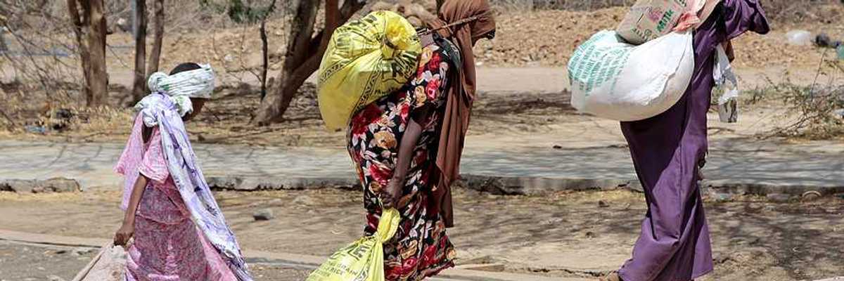 Several Somalian women carry bags of food at an African refugee camp