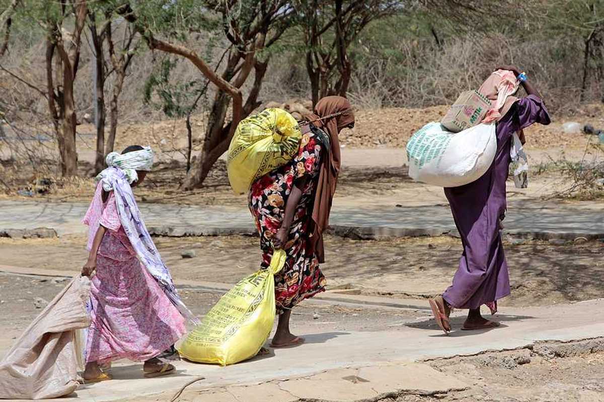 Several Somalian women carry bags of food at an African refugee camp