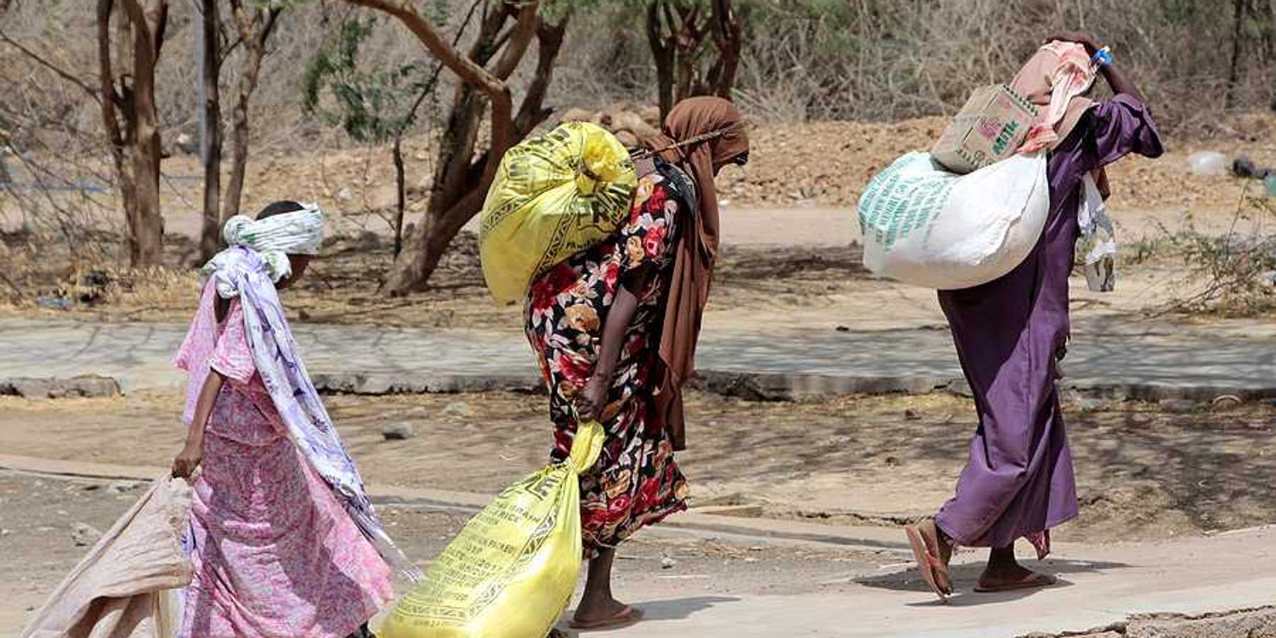 Several Somalian women carry bags of food at an African refugee camp