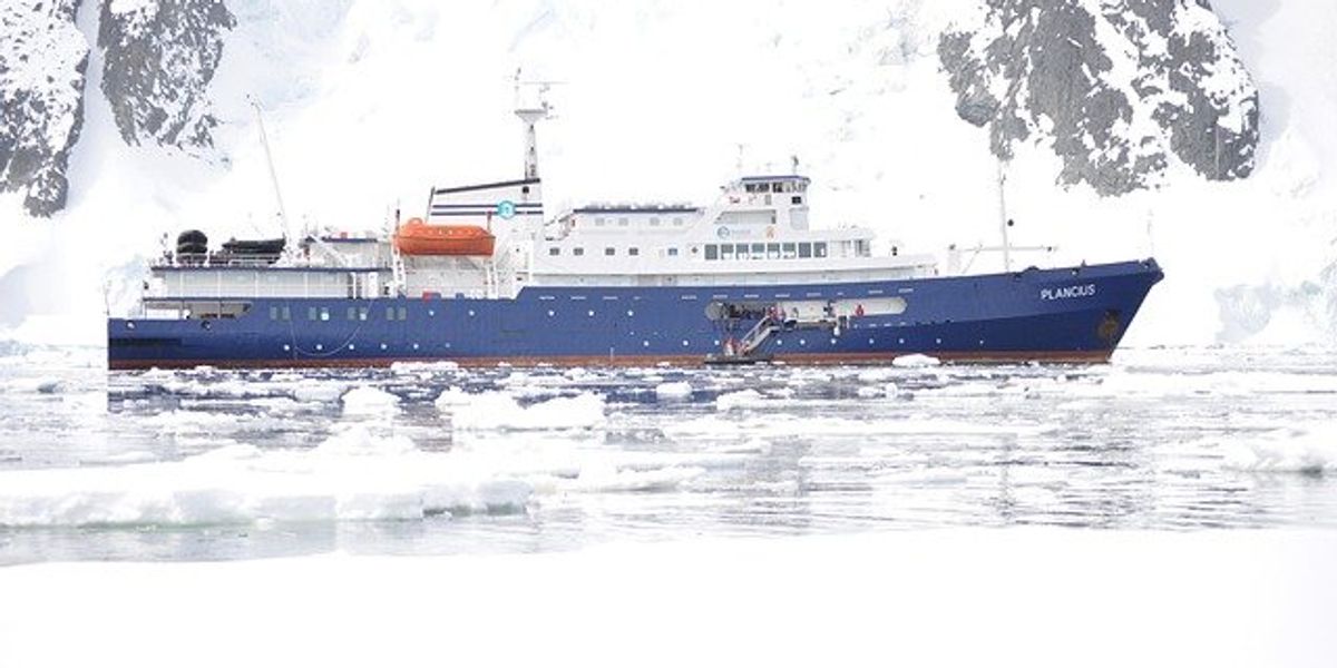 Ship floating in front of a snow-covered mountain.