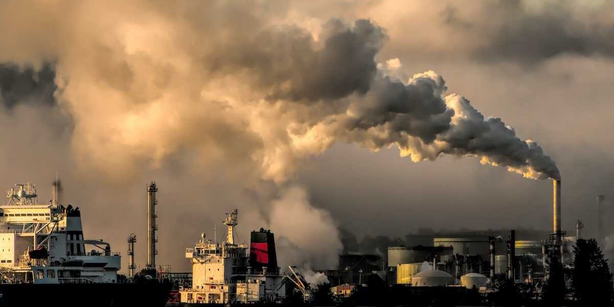 Ships in port with refinery and pollution-belching smokestack in background
