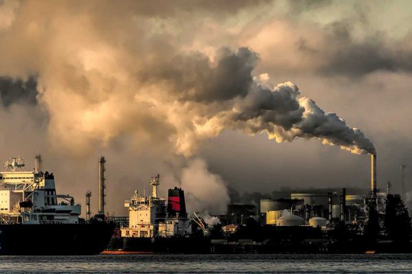 Ships in port with refinery and pollution-belching smokestack in background