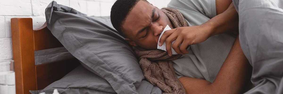 Sick African American man coughing holding paper napkin near mouth suffering from respiratory ailment