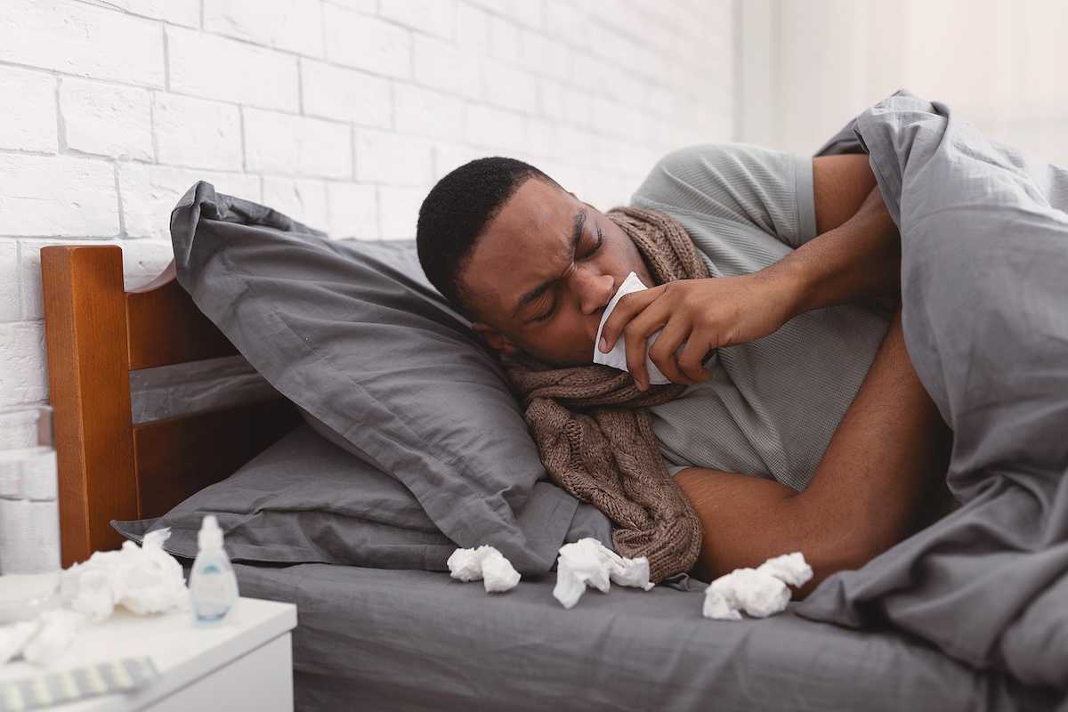 Sick African American man coughing holding paper napkin near mouth suffering from respiratory ailment