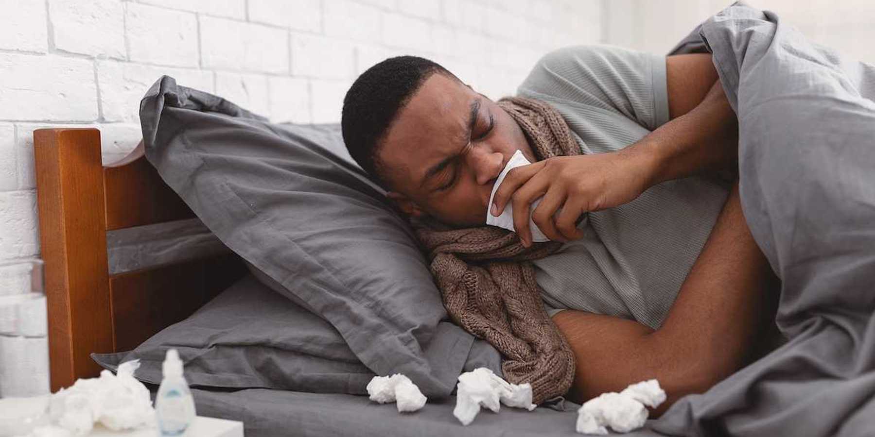 Sick African American man coughing holding paper napkin near mouth suffering from respiratory ailment