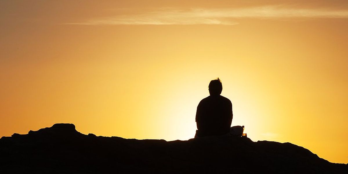 Silhouette of a person on a hill in front of a setting sun.