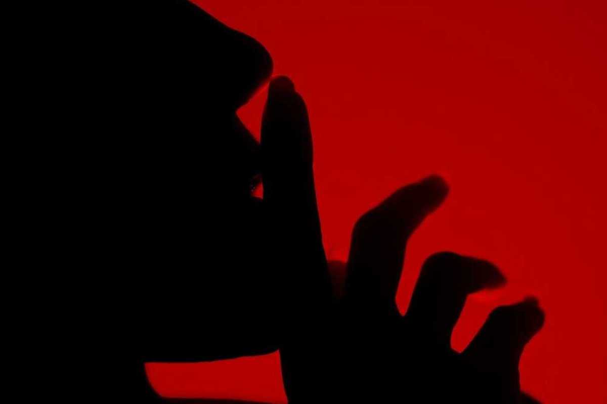 Silhouette of a person with finger to lips in a shushing gesture