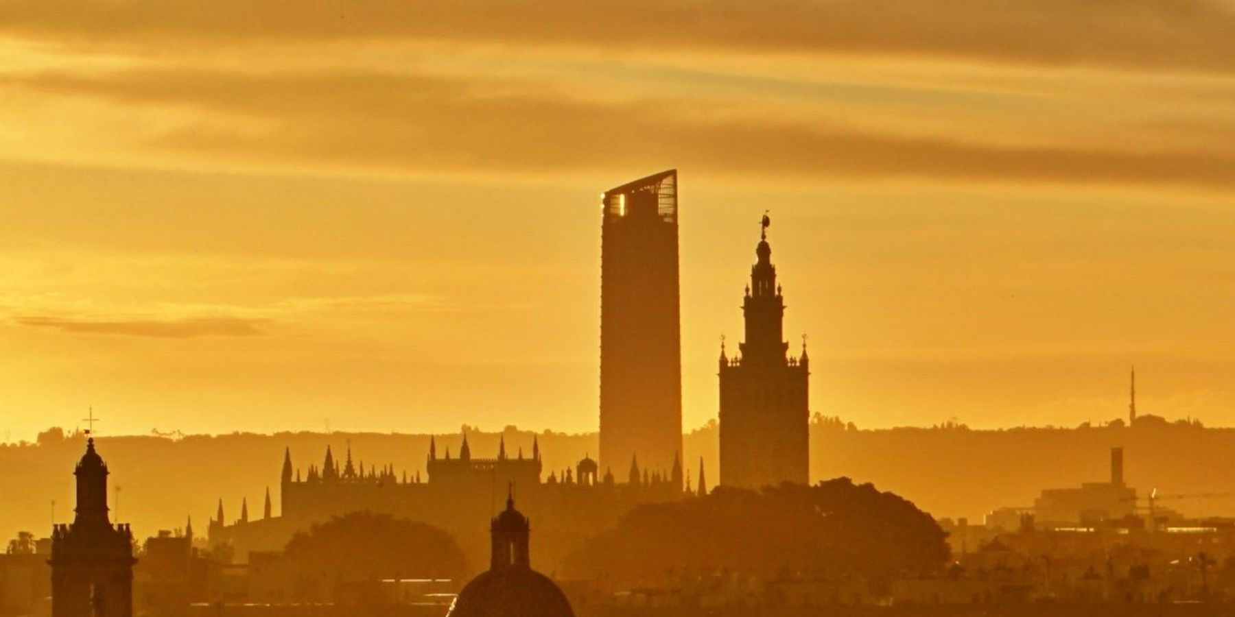 silhouette of buildings in Seville, Spain against a golden evening sky.