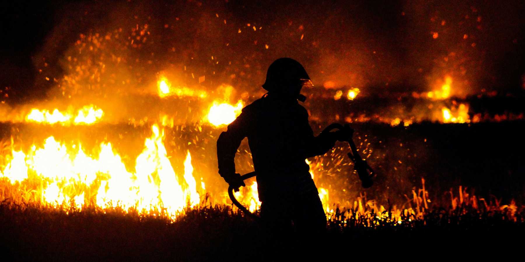 silhouette of firefighter standing on edge of wildfire during night time.