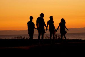 silhouette of people holding hands by a lake at sunset