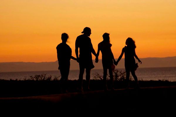 silhouette of people holding hands by a lake at sunset